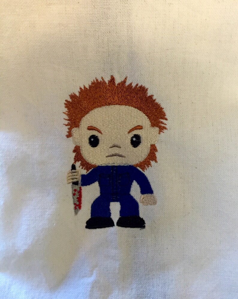 May include: An embroidered figure of a character from a horror movie, with orange hair, a blue jumpsuit, and a bloody knife. The figure has a stern expression and is set against a white background.