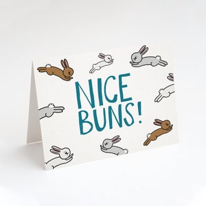 May include: A white card with a blue text that says "NICE BUNS!" surrounded by cartoon bunnies in various colors.