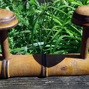 May include: A wooden coat rack with three hooks. The hooks are made of wood and have a dark brown finish. The rack is made of bamboo and has a natural finish.