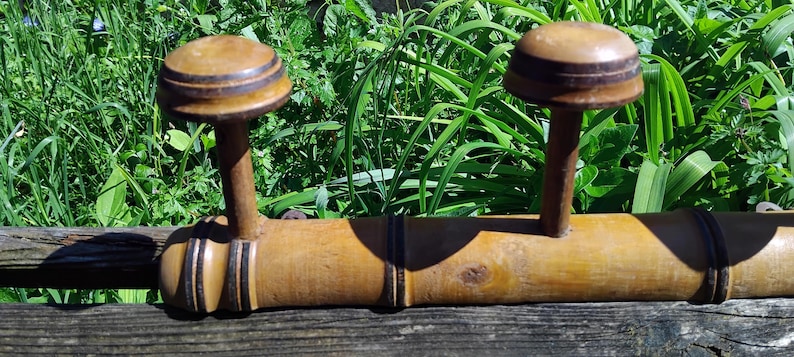 May include: A wooden coat rack with three hooks. The hooks are made of wood and have a dark brown finish. The rack is made of bamboo and has a natural finish.