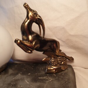 May include: A gold-toned metal sculpture of a leaping gazelle with a textured base. The sculpture is on a dark gray surface.