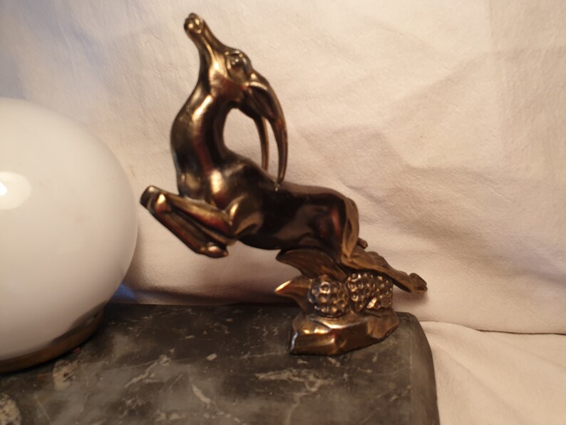 May include: A gold-toned metal sculpture of a leaping gazelle with a textured base. The sculpture is on a dark gray surface.