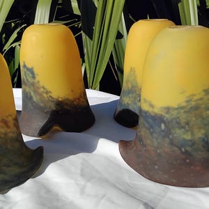 Pode incluir: Um conjunto de quatro cúpulas de vidro em forma de sino com um design degradê. A parte superior é amarelo brilhante, transitando para uma base escura manchada de azul e castanho com uma borda alargada e ondulada. Cada cúpula tem acabamento fosco.