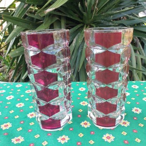 Könnte beinhalten: Zwei klare Glasvasen mit geometrischem Muster und einer tief roten Farbe. Die Vasen stehen auf einer grün-gelb gemusterten Tischdecke.