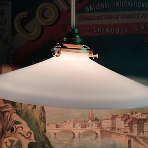 Puede incluir: Una pantalla de lámpara de vidrio blanco esmerilado cuelga de una lámpara de techo de latón y verde. La pantalla tiene forma de cuenco ancho y poco profundo. La pantalla cuelga sobre un cartel vintage con texto en francés.