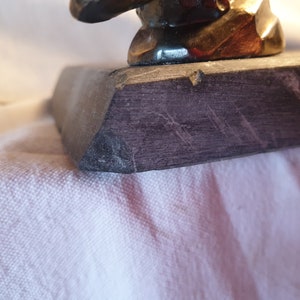 May include: Close-up of the base of a dark gray stone sculpture. The base has a rough, textured surface with visible scratches.
