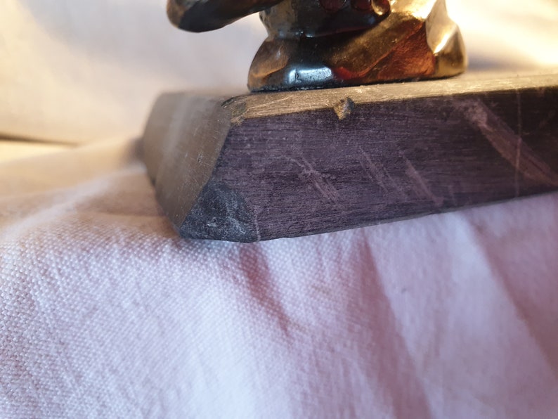 May include: Close-up of the base of a dark gray stone sculpture. The base has a rough, textured surface with visible scratches.