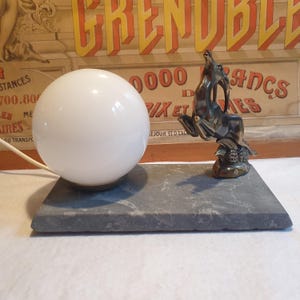 May include: A vintage table lamp with a white glass globe and a bronze deer sculpture on a gray marble base.