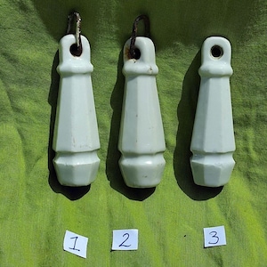 Könnte beinhalten: Drei hellgrüne Keramik-Zuggriffe mit geometrischem Design und Metallschlaufen zum Aufhängen. Die Griffe sind auf kleinen weißen Karten mit 1, 2 und 3 nummeriert. Der Hintergrund ist ein einfarbiger grüner Stoff.