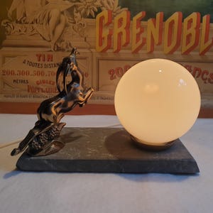 May include: A vintage table lamp with a white glass globe shade and a silver metal base featuring a stylized leaping gazelle. The base is mounted on a dark gray rectangular stone base.