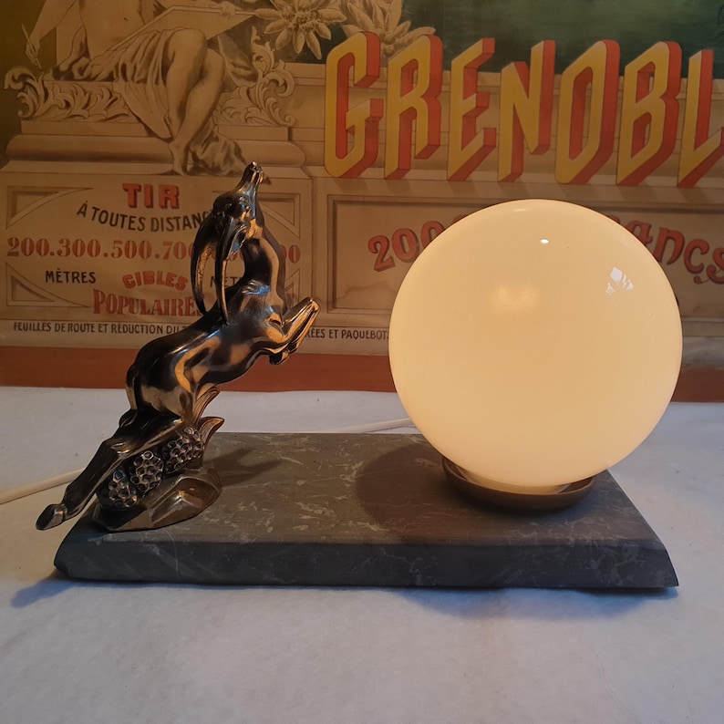 May include: A vintage table lamp with a white glass globe shade and a silver metal base featuring a stylized leaping gazelle. The base is mounted on a dark gray rectangular stone base.