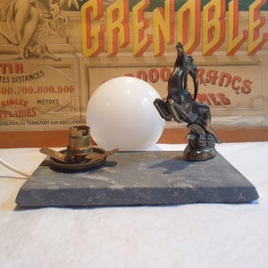 May include: A vintage table lamp with a gray marble base and a brass sculpture of a leaping antelope. The lamp has a white glass globe shade and a brass socket.