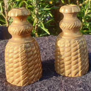 Op de afbeelding: Twee gouden metalen kaarsenstandaards met een getextureerd, geweven ontwerp. De kaarsenstandaards hebben de vorm van een kegel met een afgeronde bovenkant.