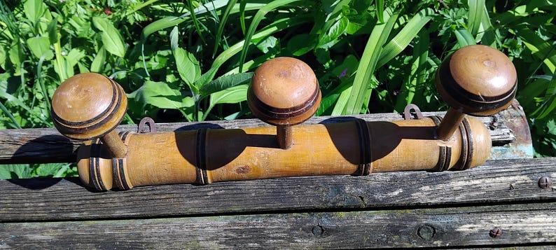 May include: A wooden coat rack with three hooks. The hooks are made of wood and have a dark brown finish. The rack is made of bamboo and has a natural finish.