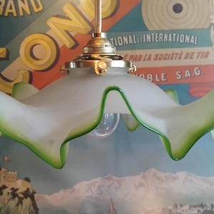 Puede incluir: Una lámpara colgante con una pantalla de vidrio esmerilado con un borde ondulado y fruncido resaltado en verde brillante. La pantalla está unida a un soporte de metal color latón pulido y una varilla central, con una bombilla visible.