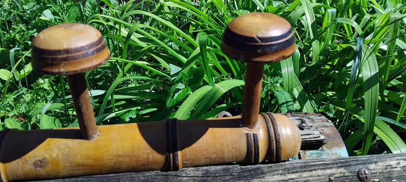 May include: A wooden coat rack with three hooks. The hooks are shaped like mushrooms with brown and black stripes. The rack is made of bamboo and has a natural finish.