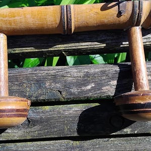 May include: A wooden coat rack with two hooks. The rack is made of natural bamboo and has a dark brown stain. The hooks are made of wood and have a black and brown striped design.