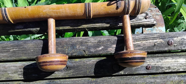 May include: A wooden coat rack with two hooks. The rack is made of natural bamboo and has a dark brown stain. The hooks are made of wood and have a black and brown striped design.