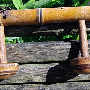May include: A wooden coat rack with three hooks, made from bamboo with a natural finish. The hooks are round and have a brown and black striped pattern.