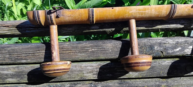 May include: A wooden coat rack with three hooks, made from bamboo with a natural finish. The hooks are round and have a brown and black striped pattern.
