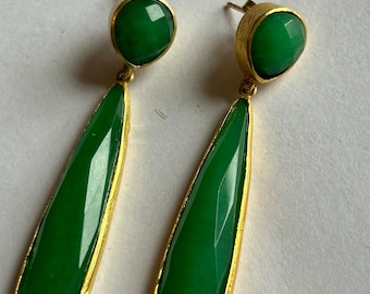 May include: A pair of green gemstone drop earrings with gold accents. The earrings feature a round green gemstone at the top and a teardrop-shaped green gemstone below.
