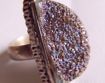 May include: A silver ring with a large, iridescent purple and blue gemstone. The gemstone is set in a silver bezel and has a textured surface.