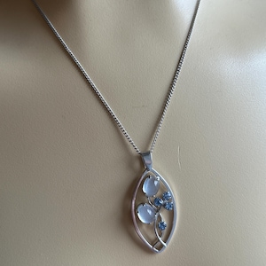 May include: A silver chain necklace with a pendant featuring a silver leaf design with two white oval stones and three blue stones.