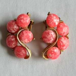 May include: A pair of clip-on earrings with a gold-tone setting and pink marbled stones. The stones are arranged in a curved shape, creating a unique and elegant design.
