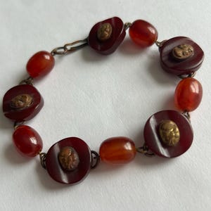 May include: A red and gold bracelet with round beads and a clasp. The beads have a raised design.