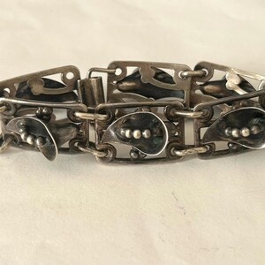 May include: A vintage silver bracelet with an intricate design. The bracelet comprises rectangular and teardrop-shaped links. Each teardrop link has small, raised dots. The bracelet is made of silver-toned metal and has a clasp closure.