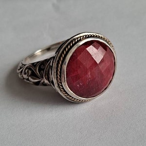 Pode incluir: Um anel de prata com um design ornamentado e uma grande gema vermelha facetada engastada em uma moldura de ouro.