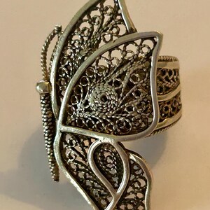 May include: A silver filigree butterfly ring. The ring is made of delicate, intricate silver wire that is woven together to create a detailed butterfly design.
