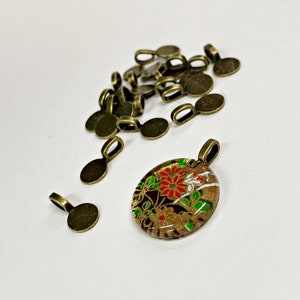 May include: A pile of 18 antique gold-toned metal pendant bails, with one bail attached to a round glass pendant with a floral design in red, green, white, and gold.