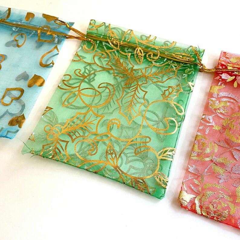 K&ouml;nnte beinhalten: Drei Organza-Geschenkbeutel mit goldenen Blumenmustern. Die Beutel sind hellblau, gr&uuml;n und rosa.