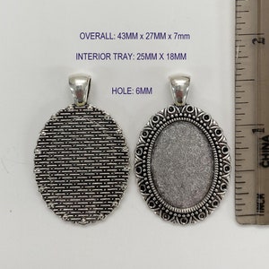 Puede incluir: Dos bandejas ovaladas de plata para colgantes con un borde decorativo. La bandeja de la izquierda tiene una superficie texturizada. La bandeja de la derecha tiene una superficie lisa. Las dimensiones totales son 43 mm x 27 mm x 7 mm. La bandeja interior es de 25 mm x 18 mm. El agujero es de 6 mm.