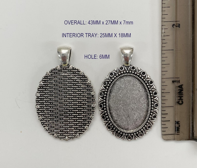 Puede incluir: Dos bandejas ovaladas de plata para colgantes con un borde decorativo. La bandeja de la izquierda tiene una superficie texturizada. La bandeja de la derecha tiene una superficie lisa. Las dimensiones totales son 43 mm x 27 mm x 7 mm. La bandeja interior es de 25 mm x 18 mm. El agujero es de 6 mm.