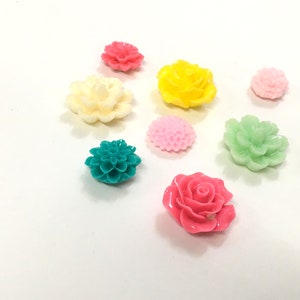 K&ouml;nnte beinhalten: Sortiment aus bunten Plastikblumenverzierungen in verschiedenen Formen und Gr&ouml;&szlig;en. Die Blumen sind in den Farben Rosa, Gelb, Gr&uuml;n, Wei&szlig; und T&uuml;rkis.