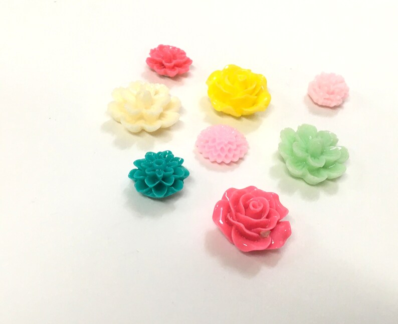 K&ouml;nnte beinhalten: Sortiment aus bunten Plastikblumenverzierungen in verschiedenen Formen und Gr&ouml;&szlig;en. Die Blumen sind in den Farben Rosa, Gelb, Gr&uuml;n, Wei&szlig; und T&uuml;rkis.