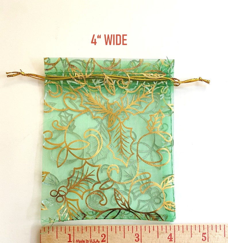 K&ouml;nnte beinhalten: Eine gr&uuml;ne, durchsichtige Kordeltasche mit goldenem Blumenmuster. Die Tasche ist 4 Zoll breit.
