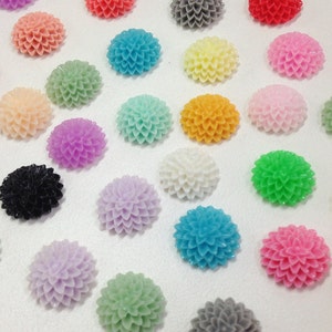 Könnte beinhalten: Sortiment von 20 bunten, blumenförmigen Cabochons. Die Cabochons sind aus Harz gefertigt und haben eine glänzende Oberfläche. Die Farben umfassen Pink, Gelb, Blau, Grün, Weiß, Schwarz und Grau.