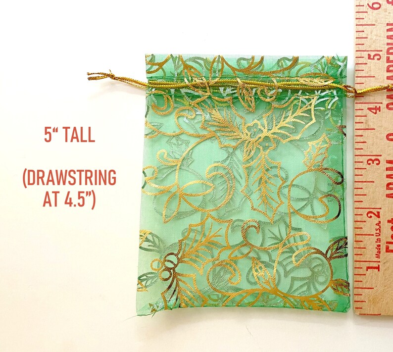 K&ouml;nnte beinhalten: Eine gr&uuml;ne Organza-Kordeltasche mit goldenem Blumenmuster. Die Tasche ist 12,7 cm hoch und hat einen Kordelzug bei 11,4 cm.