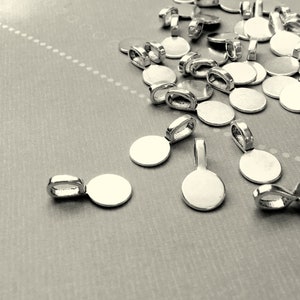 Op de afbeelding: Een stapel zilverkleurige metalen hangerbedels met ronde schijven. De bedels hebben een lus aan de bovenkant om aan een ketting of koord te bevestigen.
