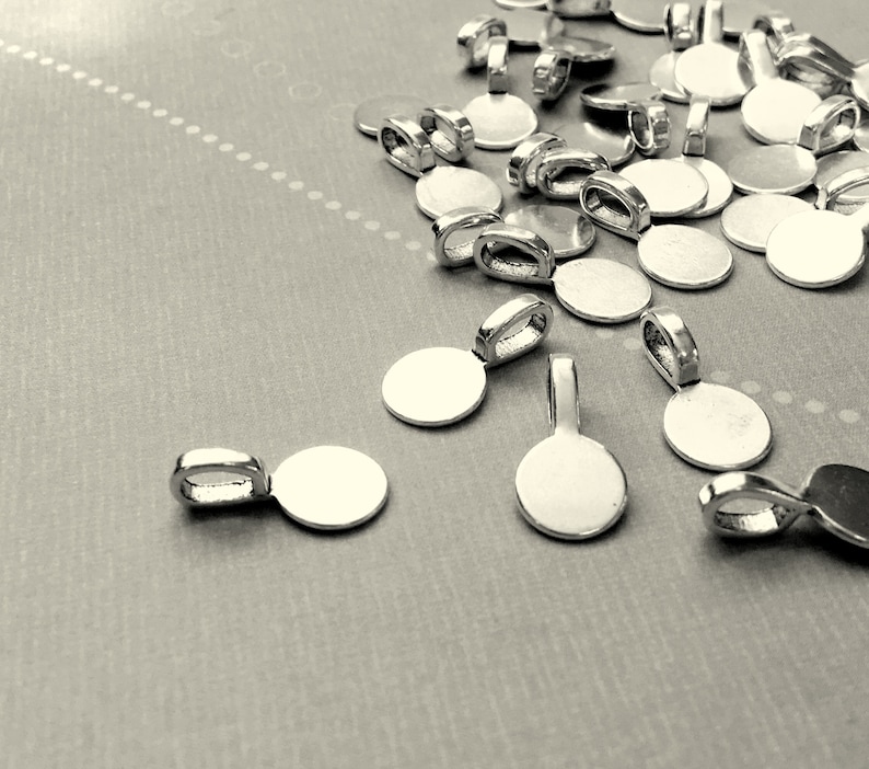 Op de afbeelding: Een stapel zilverkleurige metalen hangerbedels met ronde schijven. De bedels hebben een lus aan de bovenkant om aan een ketting of koord te bevestigen.