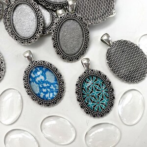 Puede incluir: Surtido de bandejas ovaladas de plata para colgantes con dise&ntilde;os ornamentados. Algunas bandejas est&aacute;n vac&iacute;as, mientras que otras presentan insertos de vidrio con patrones coloridos. Tambi&eacute;n se incluyen varios cabujones de vidrio transparente.