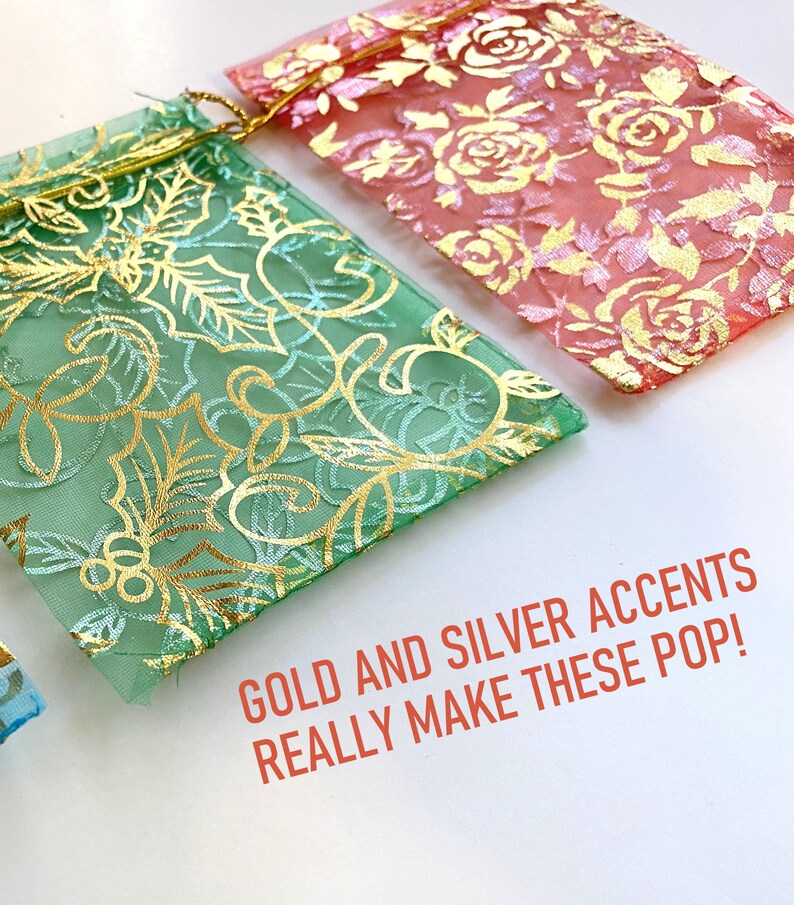 K&ouml;nnte beinhalten: Zwei durchsichtige Stoffgeschenkt&uuml;ten mit goldenen und silbernen Akzenten. Die Tasche links hat einen gr&uuml;nen Hintergrund mit einem goldenen Blumenmuster. Die Tasche rechts hat einen rosa Hintergrund mit einem goldenen Blumenmuster. Der Text "GOLD AND SILVER ACCENTS REALLY MAKE THESE POP!" steht unter den Taschen.