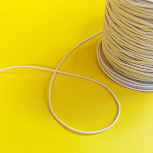 May include: A spool of off-white string or cord on a yellow background. The string is unwinding from the spool and forming a loop.