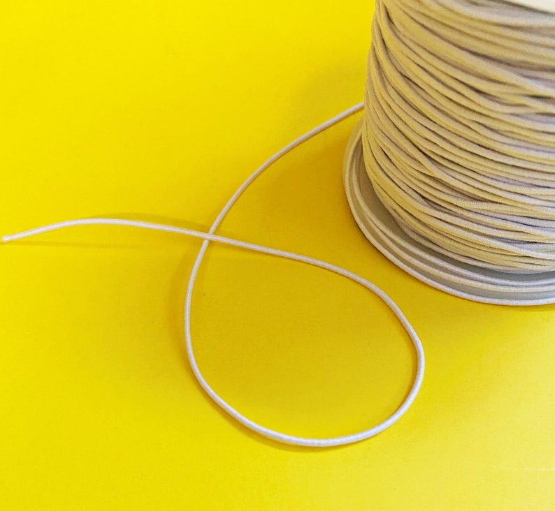 May include: A spool of off-white string or cord on a yellow background. The string is unwinding from the spool and forming a loop.