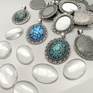 Puede incluir: Surtido de bandejas ovaladas de plata para colgantes con bordes decorativos, algunas con inserciones de vidrio con patrones azules y turquesa, y cabujones de vidrio transparentes.