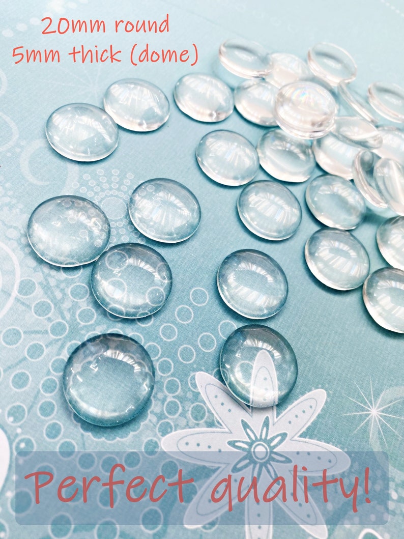 K&ouml;nnte beinhalten: Nahaufnahme einer Gruppe von transparenten Glascabochons, 20 mm rund und 5 mm dick, auf einem blauen Hintergrund mit wei&szlig;em Punktmuster. Die Cabochons sind in einem zuf&auml;lligen Muster angeordnet und einige &uuml;berlappen sich. Der Text "Perfect quality!" ist in Rot am unteren Rand des Bildes geschrieben.
