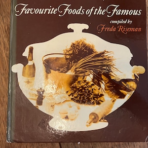 Puede incluir: Un libro marrón con el título "Favourite Foods of the Famous" y el texto "compilado por Freda Riseman". La portada presenta una ilustración estilizada de un tazón de comida con una botella de vino, hierbas y un rodillo.